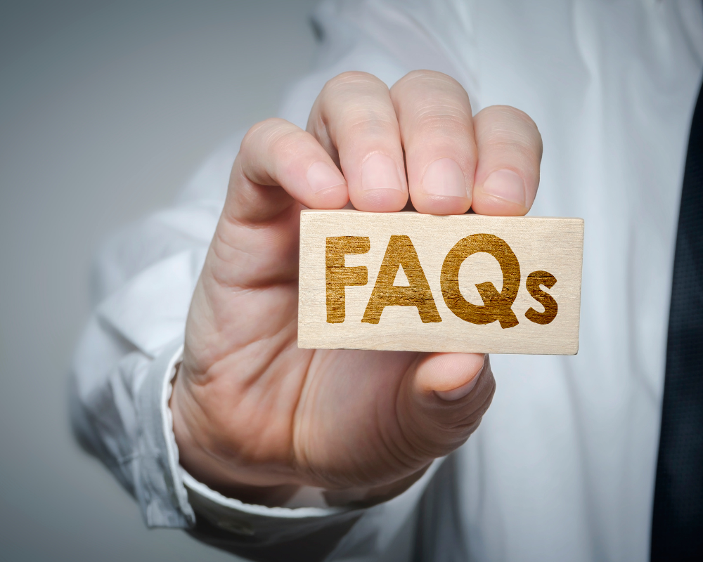 A close-up of a hand holding a wooden block engraved with the word "FAQs" in bold letters.