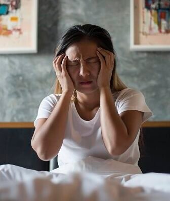 Woman sitting on bed holding her head in pain showing stress and anxiety symptoms requiring Anxiety Treatment in Bhopal