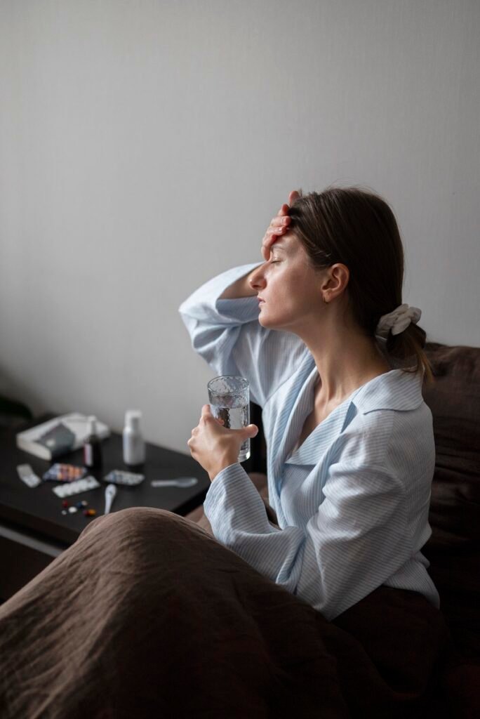 Tired woman sitting on bed holding a glass of water and touching her forehead showing stress and insomnia symptoms needing Insomnia Treatment in Bhopal