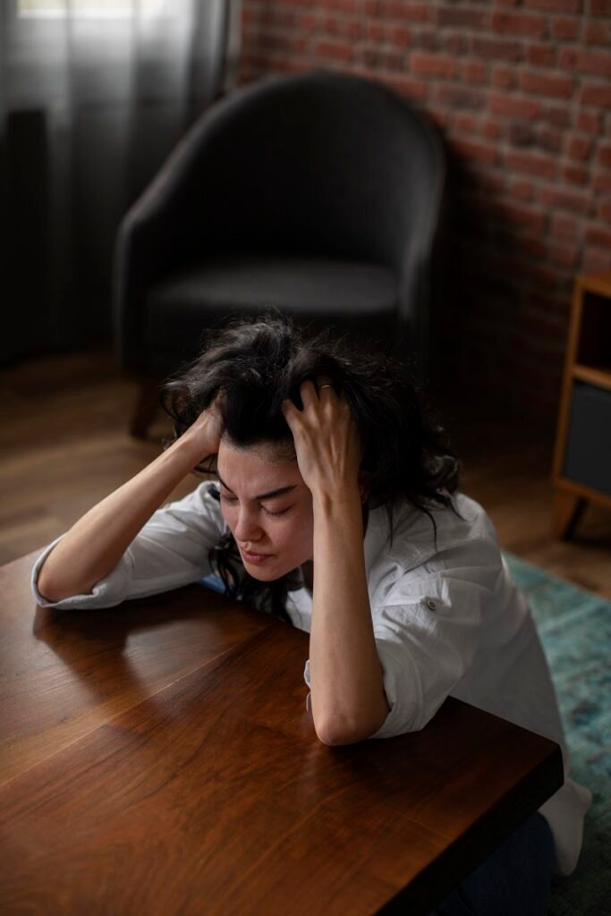 Anxious woman sitting at table holding her head showing severe stress and emotional exhaustion needing Anxiety Treatment in Bhopal