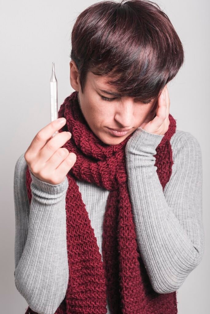 Woman holding thermometer and touching her head showing fever and illness symptoms requiring medical consultation and treatment in Bhopal